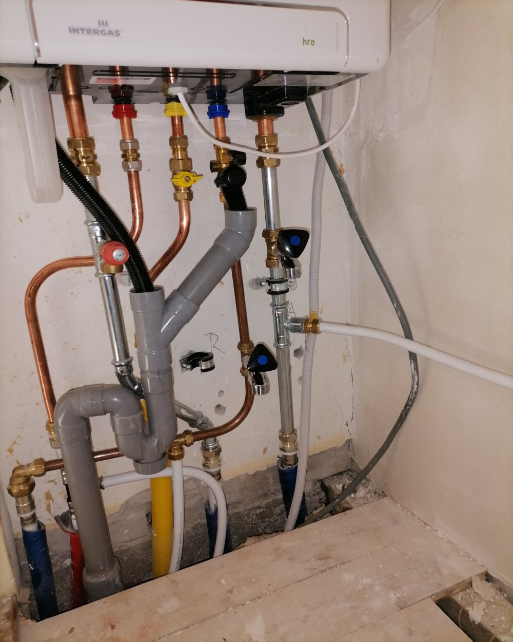 Nowa instalacja grzewcza z kotłem Intergas, widoczne rury miedziane, zawory z niebieskimi i żółtymi uchwytami, szare rury PCV odprowadzające skropliny, oraz białe i niebieskie rury doprowadzające...