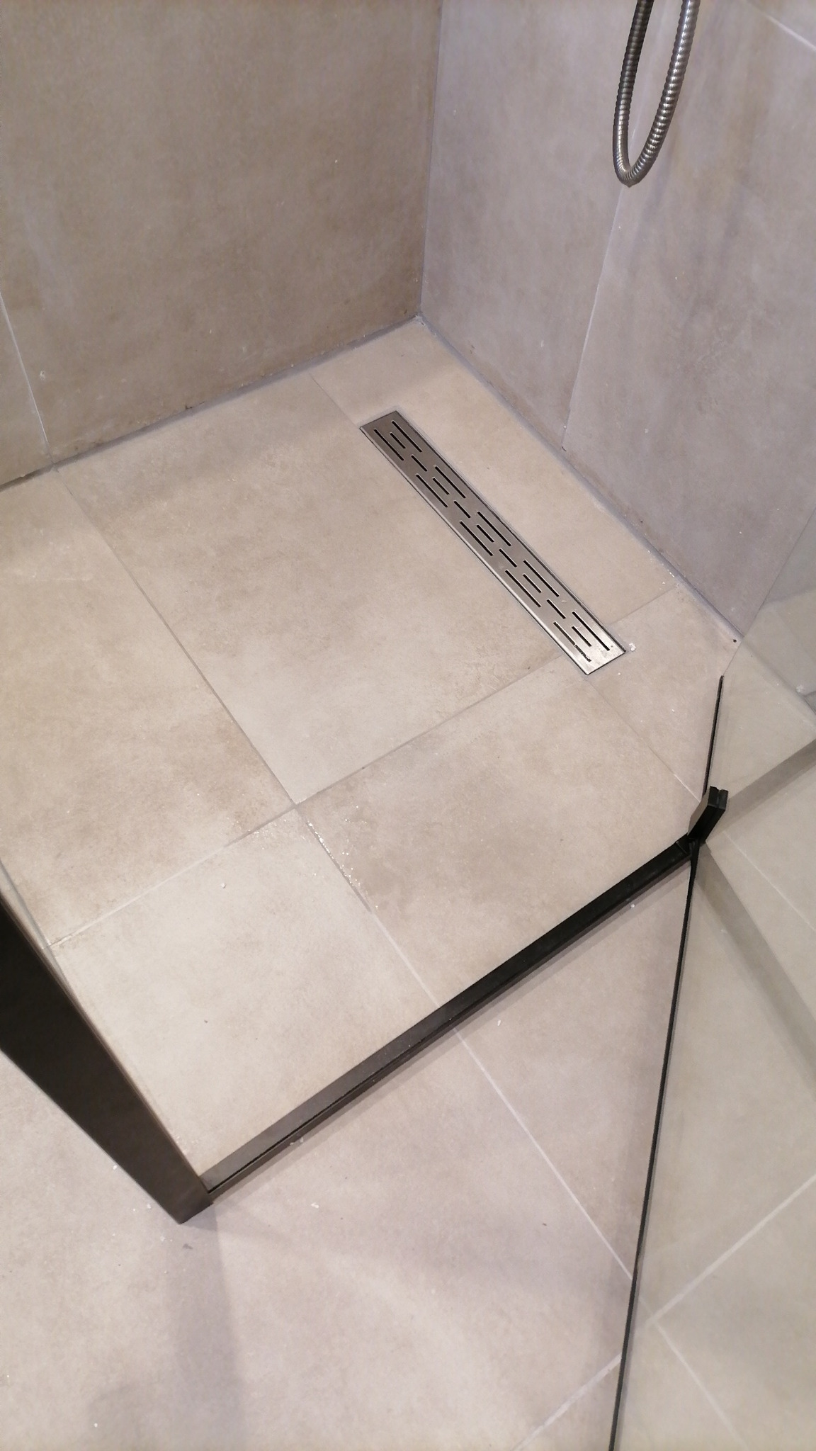 Nowoczesny odpływ liniowy ze stali nierdzewnej w kabinie prysznicowej z beżowymi płytkami, zrealizowany w miejscowości Cuijk.