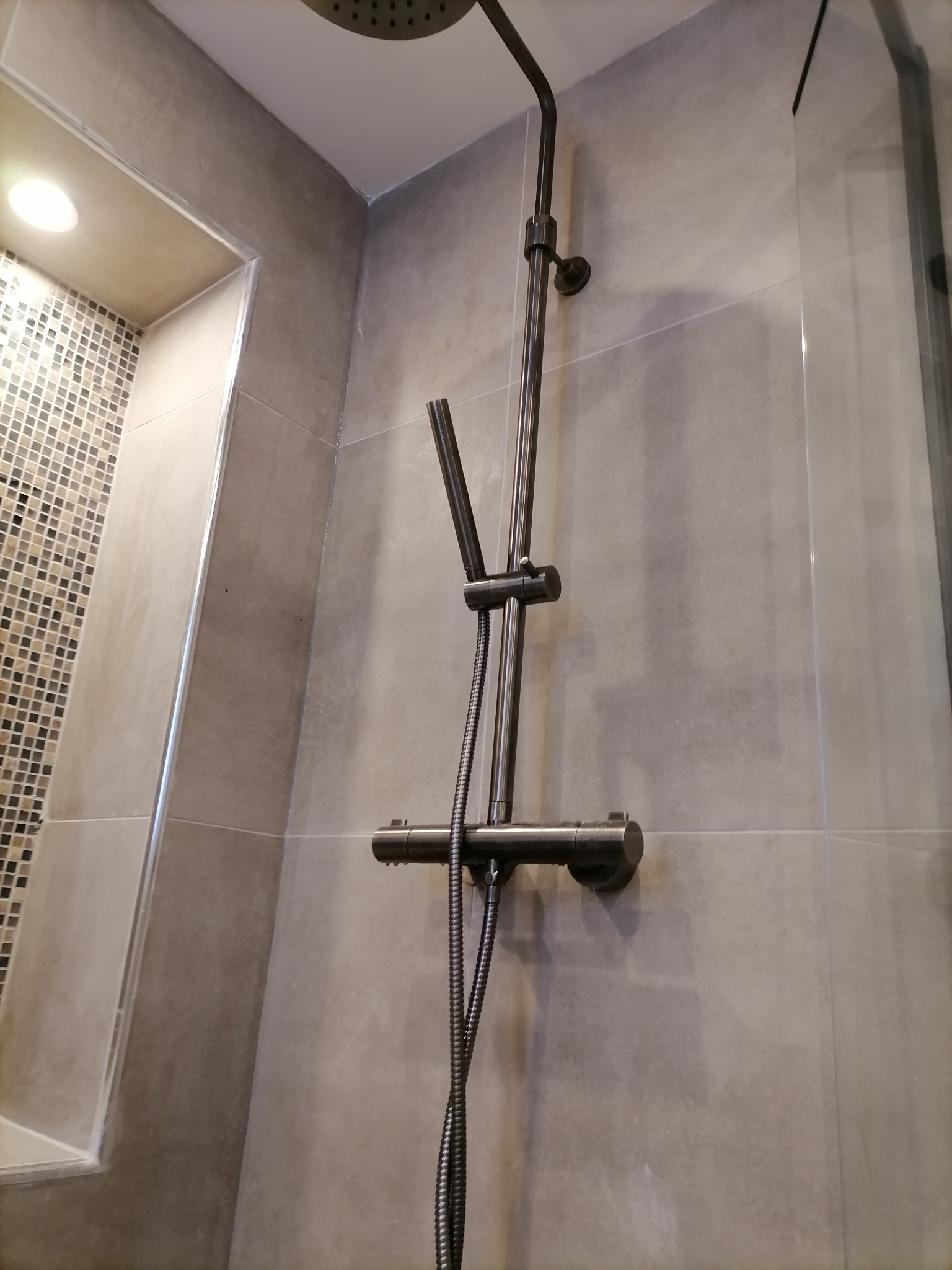 Szara kabina prysznicowa z deszczownicą i baterią termostatyczną, wykończona mozaiką w niszy.