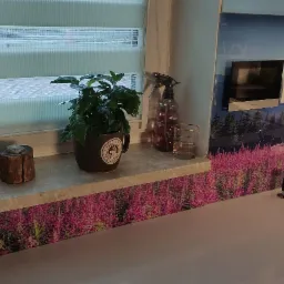 Nowoczesna kuchnia z blatem i ścianą ozdobioną motywem kwitnących wrzosów, zlew z czarną armaturą i rośliny doniczkowe na parapecie.