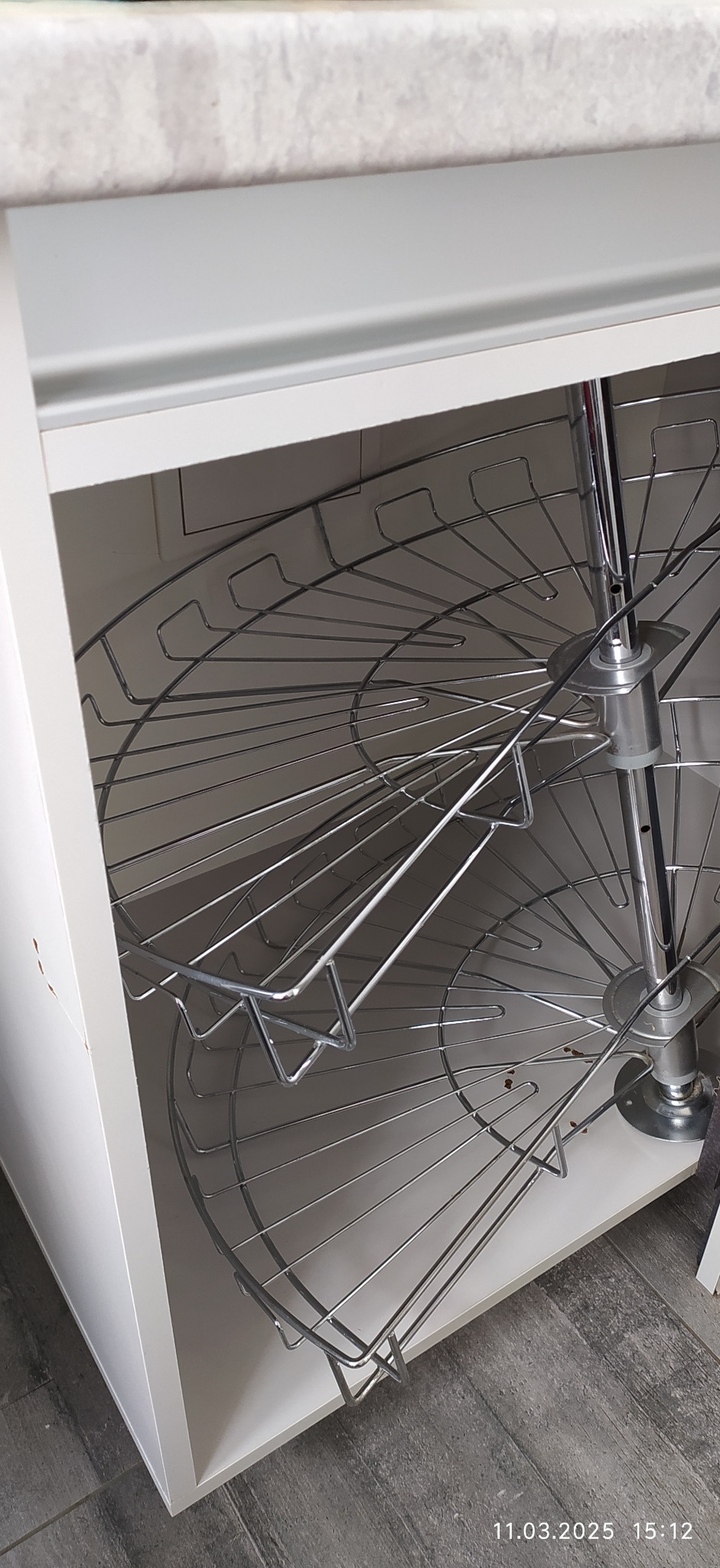 Wnętrze białej szafki narożnej z dwupoziomową, chromowaną karuzelą na naczynia, widoczne ślady użytkowania.
