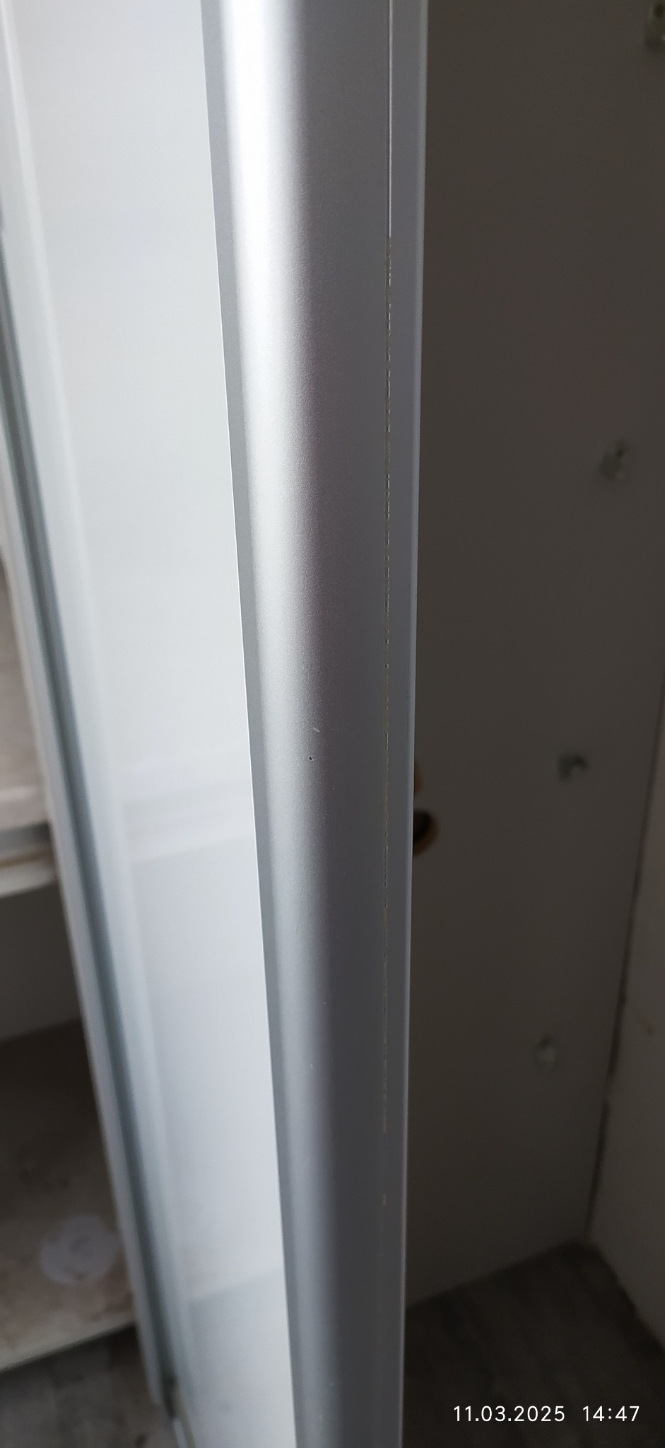 Detail of a newly installed, silver shower enclosure frame, showing the clean lines and tight seal against the wall, with faint traces of construction dust visible.