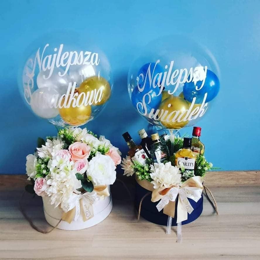 Dwa eleganckie kosze prezentowe: jeden biały z kwiatami i balonem z napisem 'Najlepsza Świadkowa', drugi granatowy z miniaturowymi butelkami alkoholu, kwiatami i balonem z napisem 'Najlepszy Świadek'.