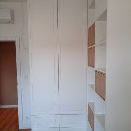 Rivej Sergii Yatsunov - Biała szafa wnękowa z frezowanymi frontami i drewniane półki otwarte, tworzące geometryczny wzór. Widok na fragment podłogi i drzwi.