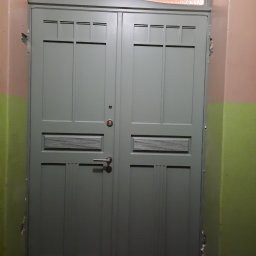 Rivej Sergii Yatsunov - Szare, dwuskrzydłowe drzwi wewnętrzne z nadświetlem w korytarzu z uszkodzeniami ścian. Drzwi posiadają charakterystyczne zdobienia i skrzynkę na listy.