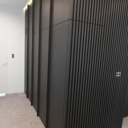 Rivej Sergii Yatsunov - Nowoczesna, szara szafa wnękowa z lamelami i gładkimi frontami, wkomponowana w jasne wnętrze z widocznymi elementami instalacji elektrycznej.