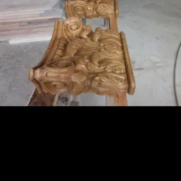 Dwa ozdobne, lakierowane elementy drewniane z rzeźbieniami leżące na stole w warsztacie, prawdopodobnie fragmenty balustrady lub schodów.