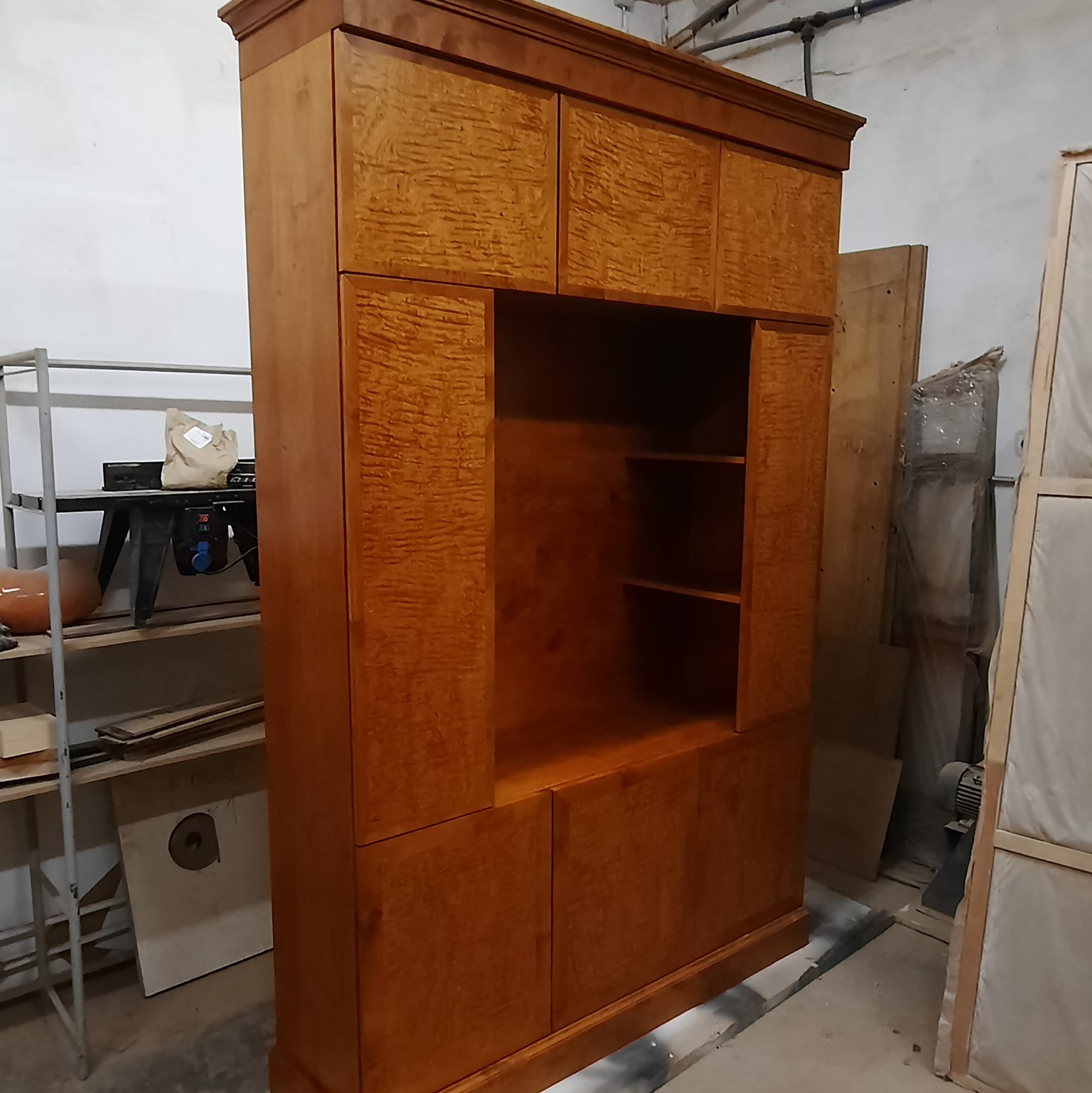 Masywna, fornirowana szafa z otwartą półką, wykonana na zamówienie. Widoczne detale wykończenia i struktura drewna. Szafa stoi w warsztacie.