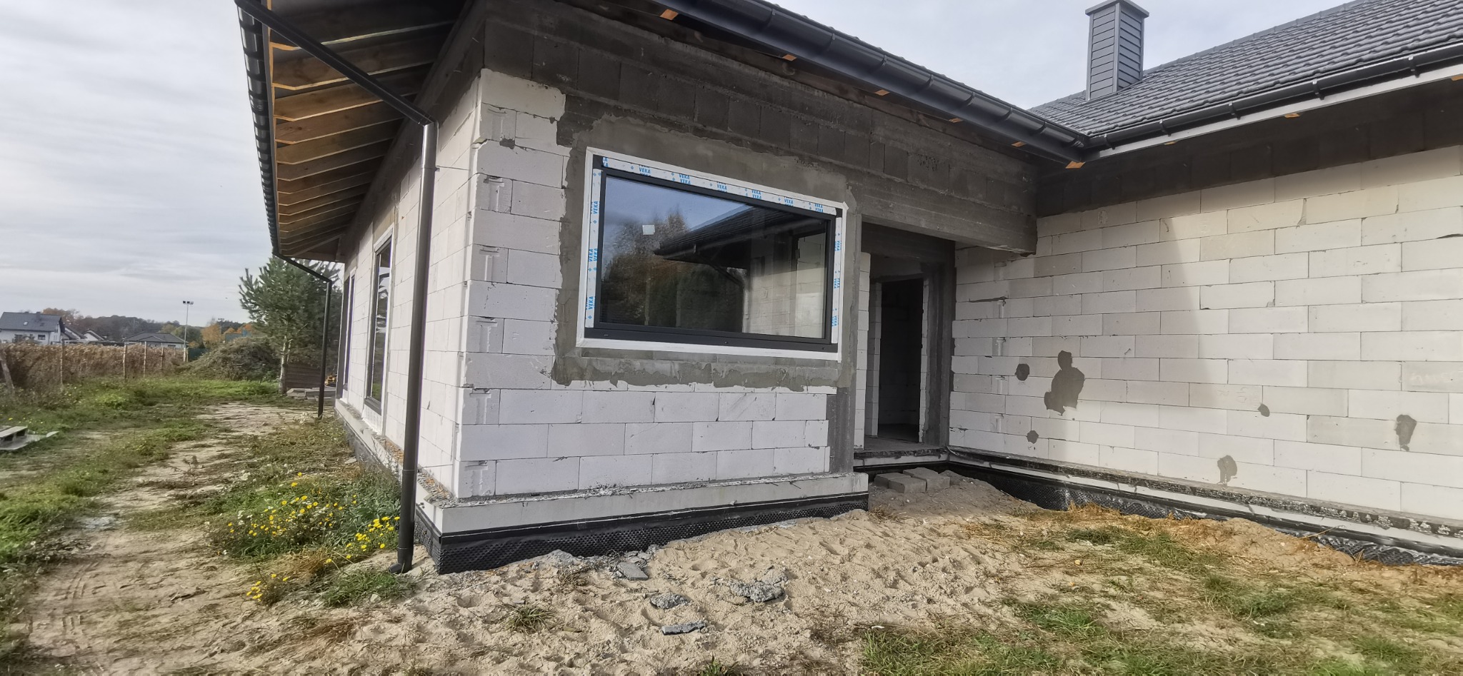 Montaż okna w surowym stanie budynku z białych bloczków, widoczne taśmy uszczelniające na oknach.