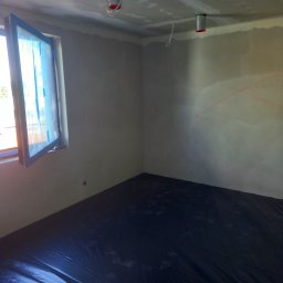 Usługi remontowe - Pokój w trakcie przygotowań do prac wykończeniowych, z zabezpieczoną folią podłogą i oknem oklejonym taśmą malarską, ściany wstępnie przygotowane, widoczne przewody oświetleniowe.