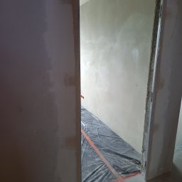 Usługi remontowe - Przygotowanie do prac wykończeniowych: zabezpieczona folią podłoga w przejściu drzwiowym, ściany w trakcie nakładania gładzi, widoczne niedoskonałości powierzchni.