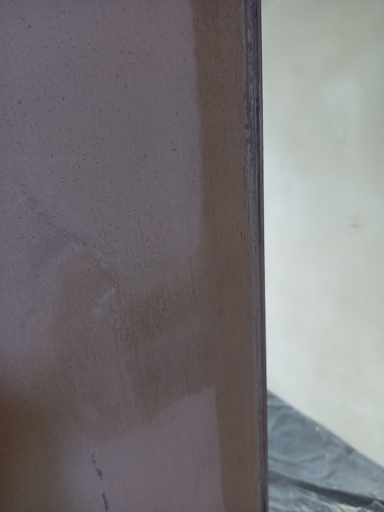 Fragment ściany z nierówną, szpachlowaną powierzchnią w odcieniach beżu i brązu, widoczny z bliska, z widocznymi drobnymi nierównościami i smugami, obok fragmentu białej ściany i zabezpieczonej...