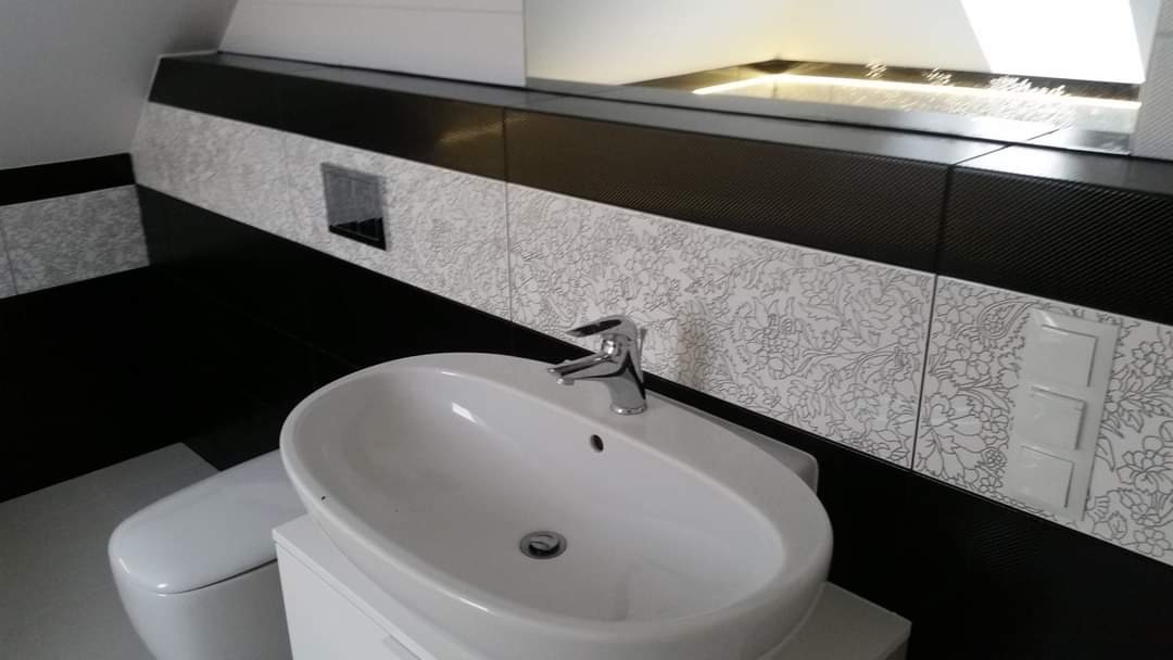 Biała, owalna umywalka nablatowa z chromowaną baterią na tle czarno-białych płytek z motywem kwiatowym w nowoczesnej łazience.