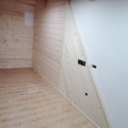 STAN-DACH Stanisław Łuszczek - Wnętrze pokoju z drewnianą boazerią na ścianach, drewnianymi belkami stropowymi, panelami podłogowymi i częściowo wykończoną ścianą z gipsu z puszkami elektrycznymi.