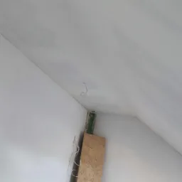 Poddasze z ukośnym sufitem w trakcie wykańczania, widoczne płyty OSB oparte o ścianę oraz narzędzia do obróbki drewna na blacie roboczym