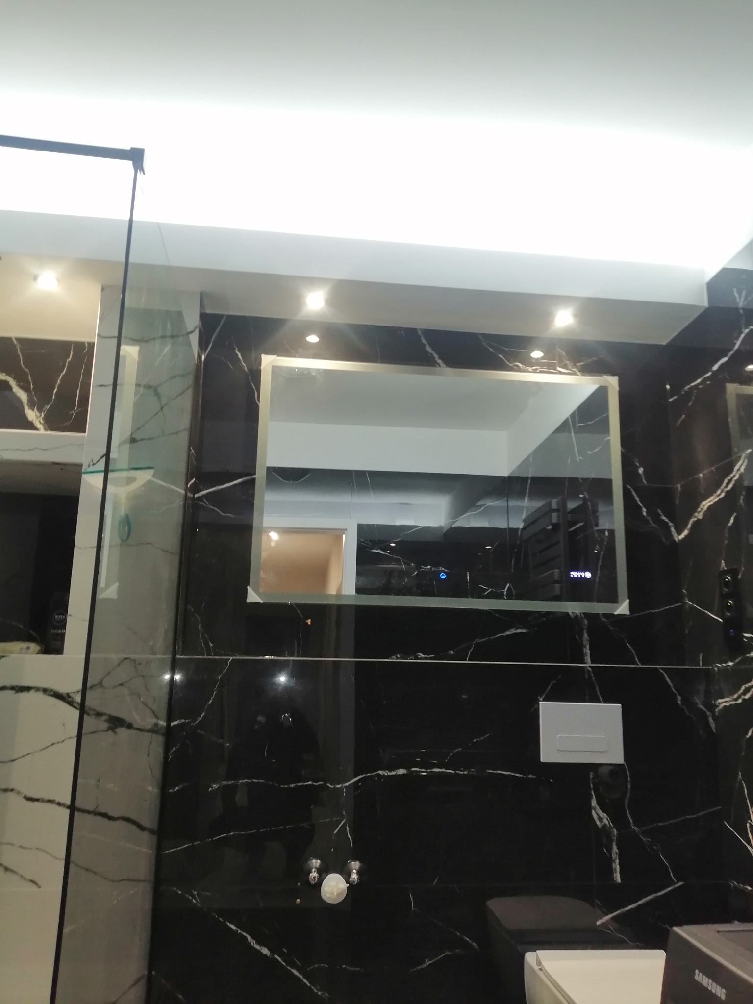 Nowoczesna łazienka z czarnymi płytkami imitującymi marmur, podświetlanym lustrem i minimalistyczną armaturą.