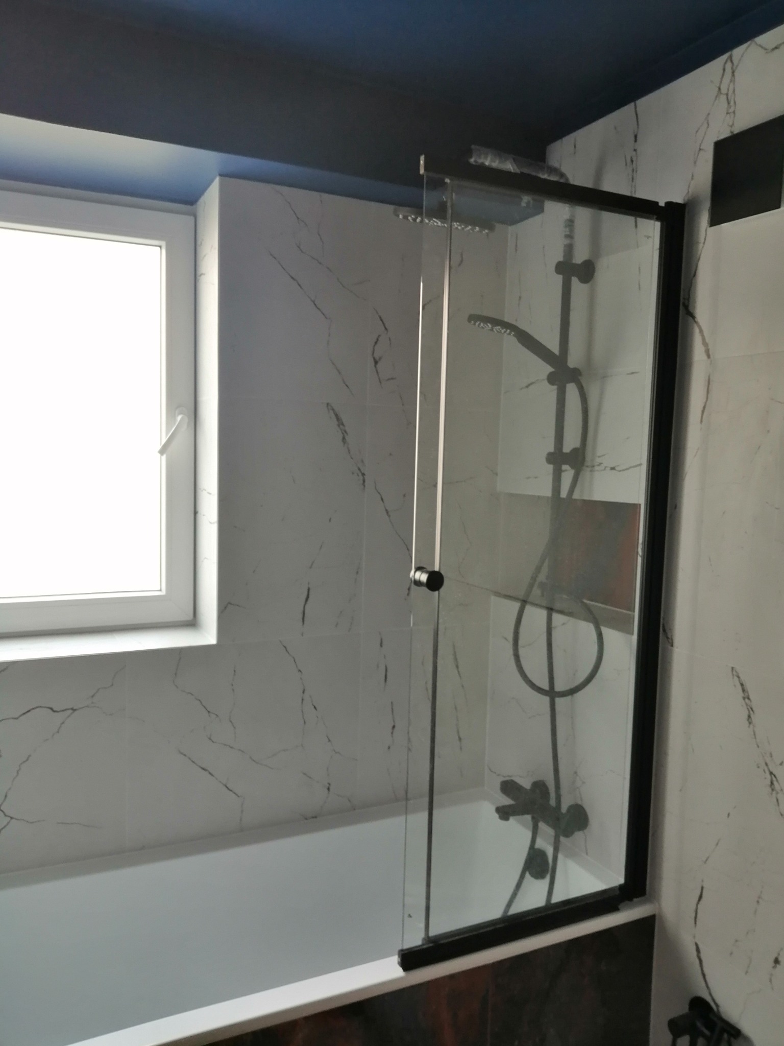 Nowoczesna łazienka z biało-szarymi marmurkowymi płytkami, kabiną prysznicową z czarną ramą i deszczownicą, oraz granatowym sufitem.