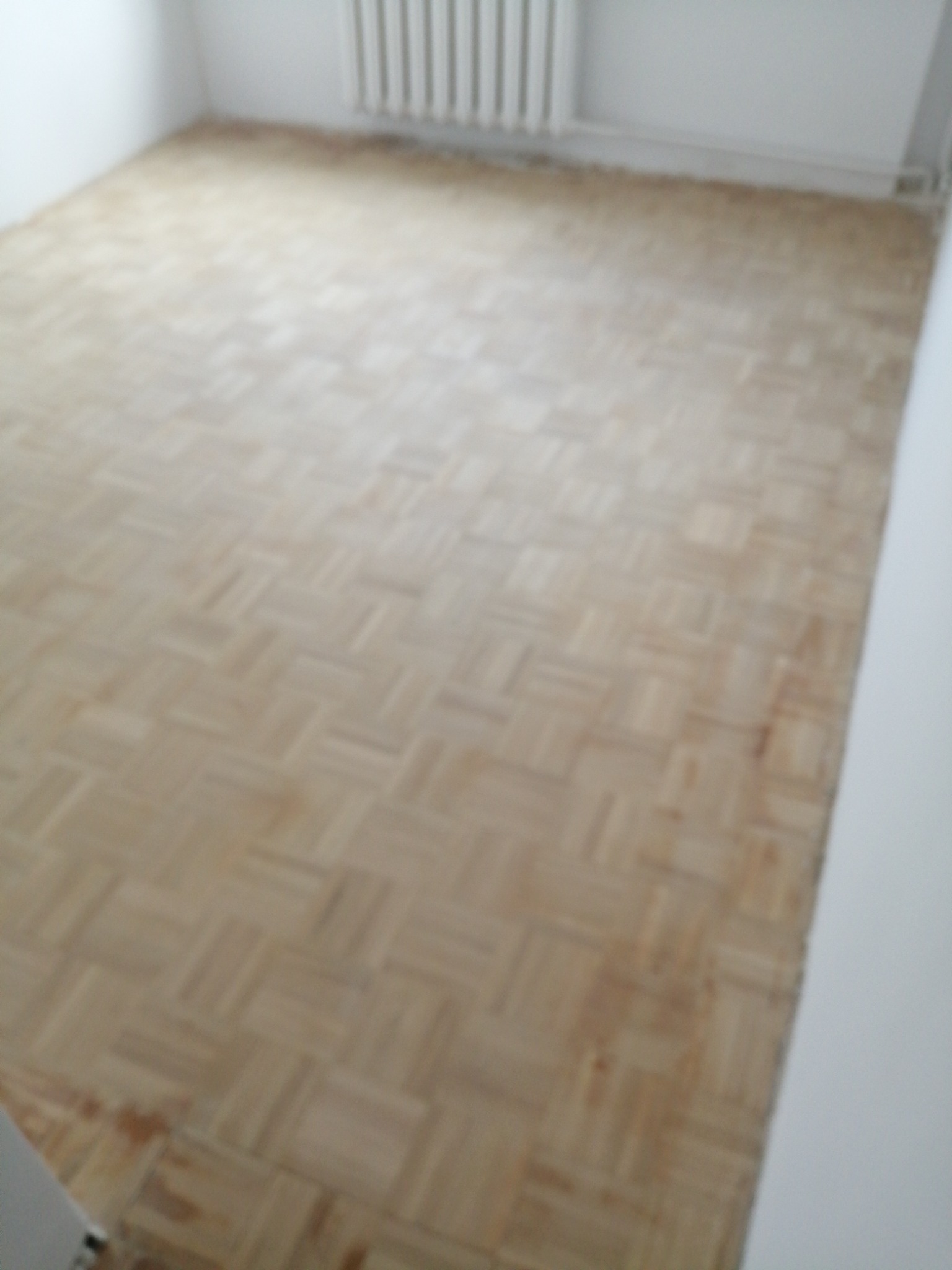 Pokój przed remontem z parkietem w jodełkę, widoczne ślady użytkowania i zabrudzenia, grzejnik na ścianie.