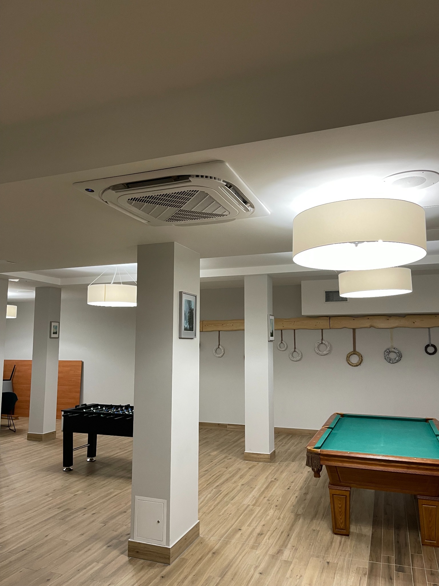 Kasetonowa jednostka klimatyzacyjna Carrier zamontowana w suficie jasnego pomieszczenia rekreacyjnego z bilardem i piłkarzykami.