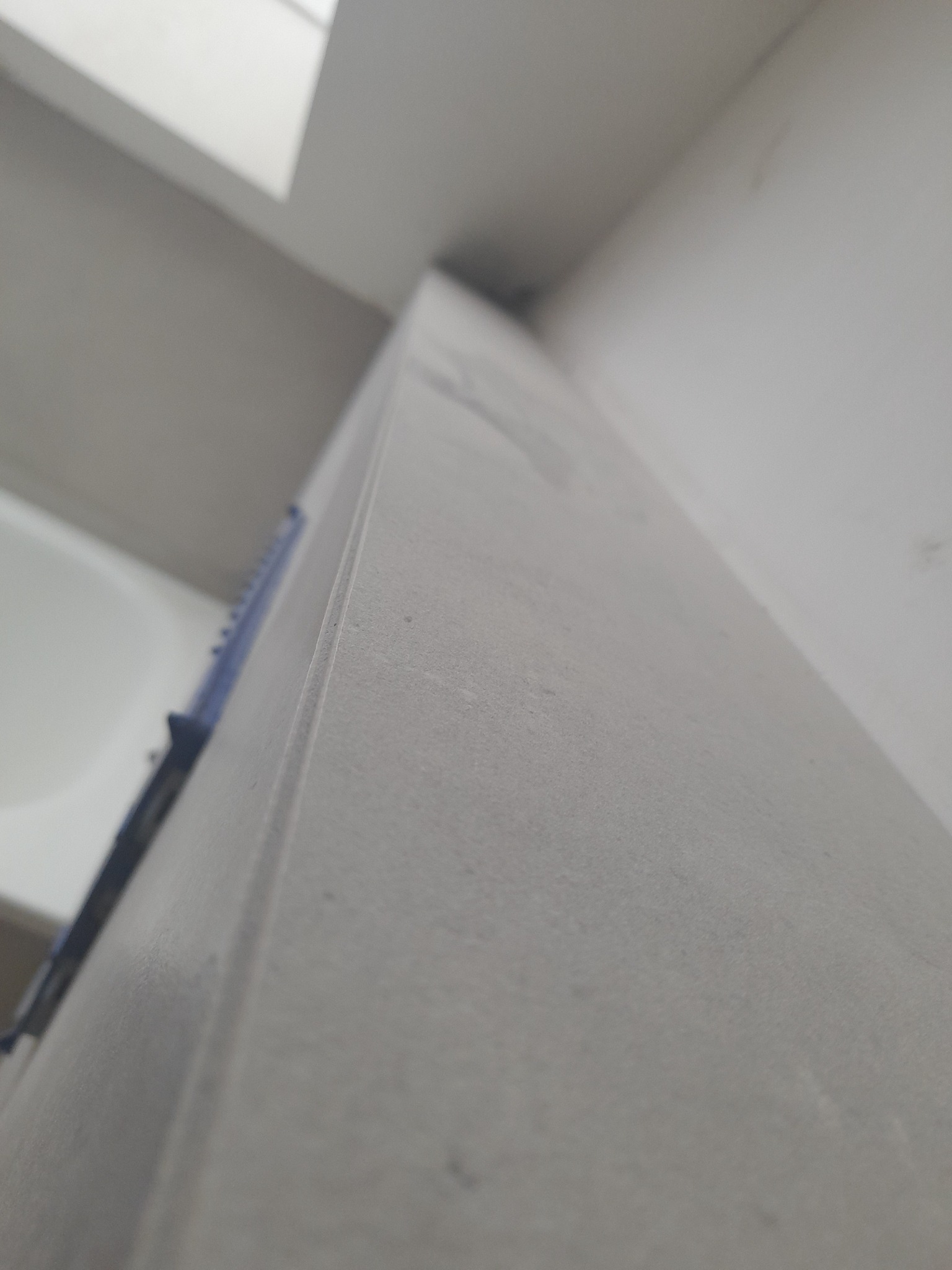 Narożnik ściany w łazience wykończony szarą płytką ceramiczną, zabezpieczony niebieską taśmą malarską, widok z dołu.