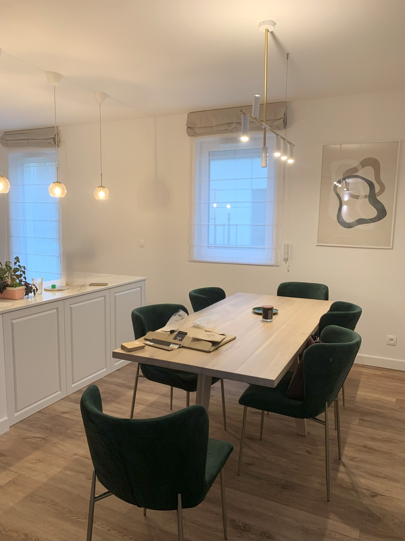 Jadalnia w Gdańsku z drewnianym stołem, zielonymi krzesłami i minimalistycznym oświetleniem. Nowoczesny design wnętrza z elementami dekoracyjnymi.