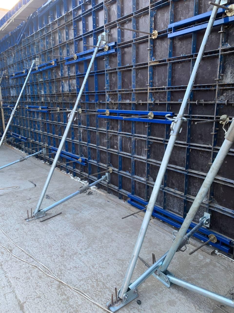 Szare fundamenty w trakcie wylewania z szalunkiem z niebieskimi elementami wzmacniającymi i metalowymi podporami.