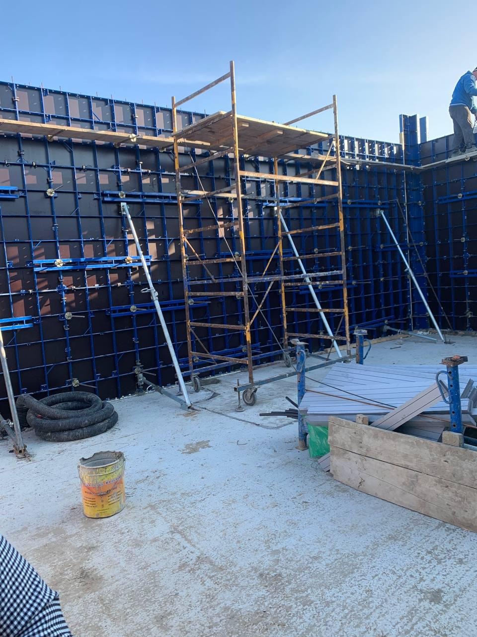 Budowa fundamentów domu: szalunek z metalowymi wzmocnieniami, rusztowanie i wiadro na placu budowy w słoneczny dzień.