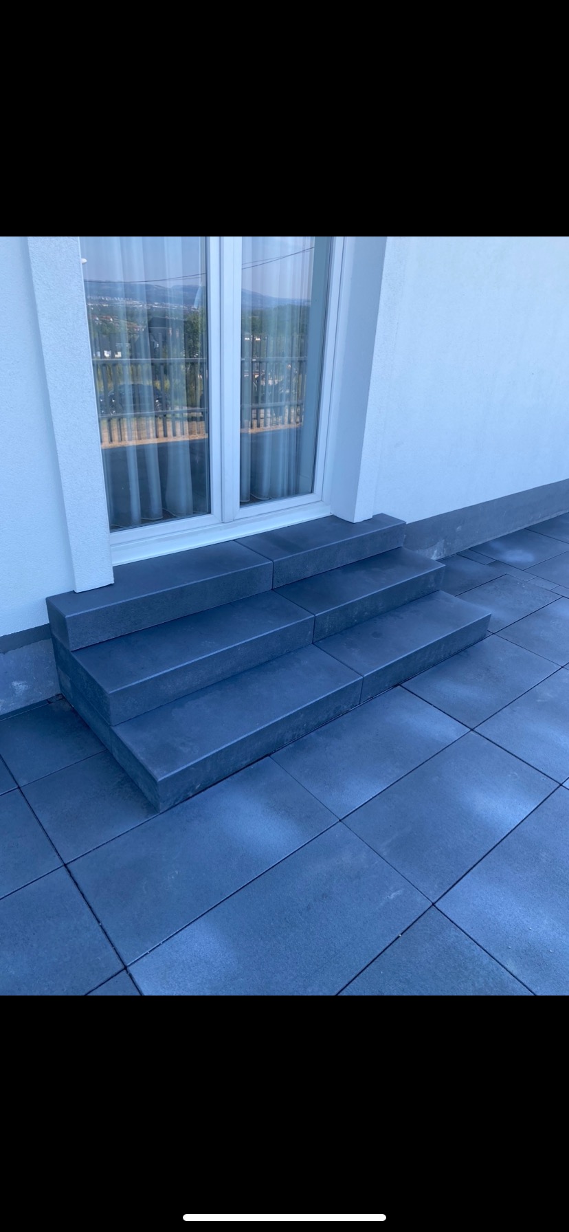 Nowoczesne, grafitowe schody wejściowe z kostki brukowej prowadzące do okna, z widokiem na miasto w tle.