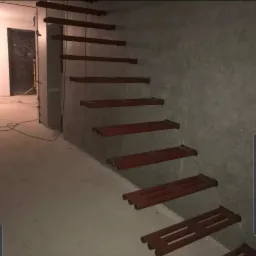 Ściana wykończona spiekiem kwarcowym w dużym formacie z zamontowanymi drewnianymi stopniami schodów, widoczne otwory montażowe, surowy stan wykończenia wnętrza.