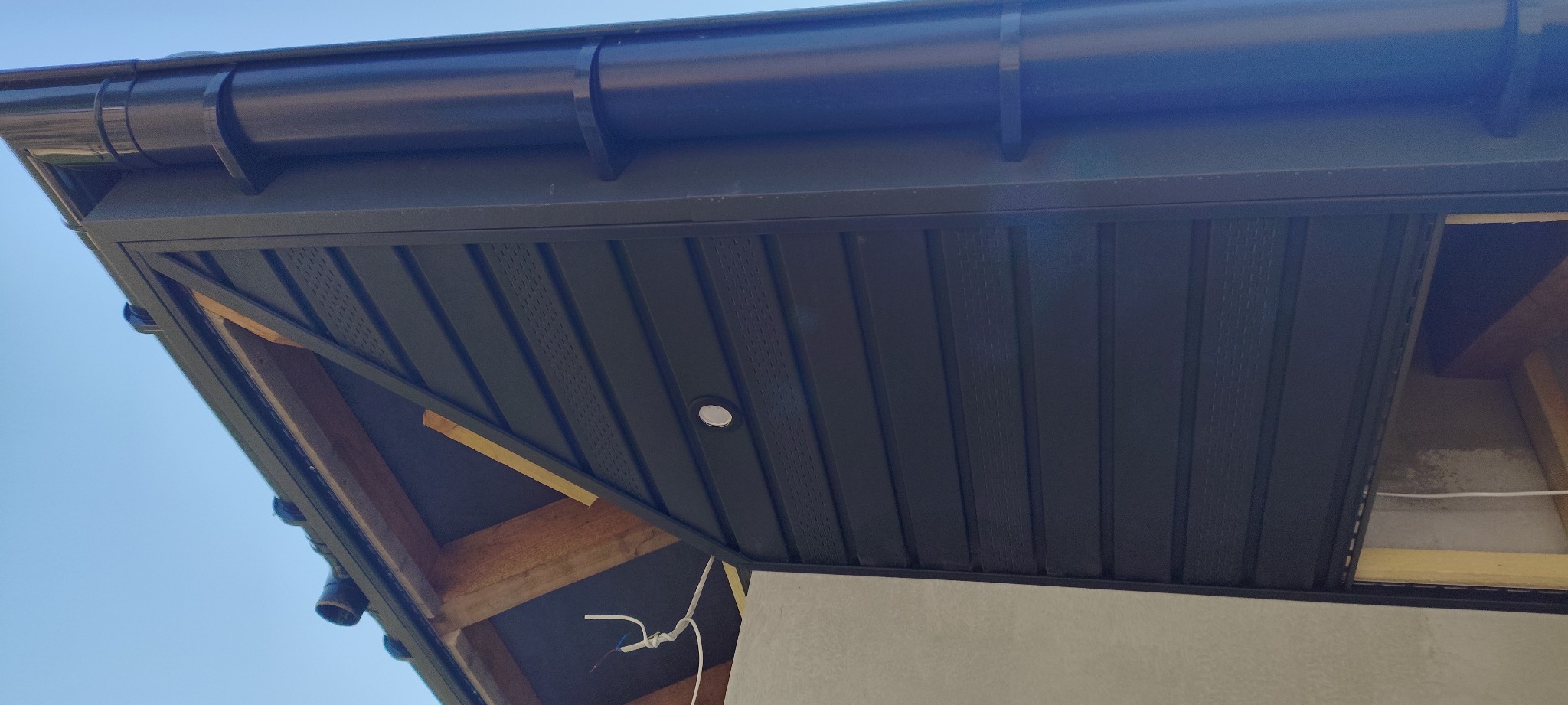 Ciemna podbitka dachowa z oświetleniem punktowym, widok z dołu, fragment konstrukcji drewnianej i orynnowanie. Detal wykończenia.