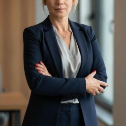 ARMADA - Portret kobiety w granatowym garniturze, skrzyżowane ręce, subtelna biżuteria, naturalne światło, profesjonalny wizerunek.