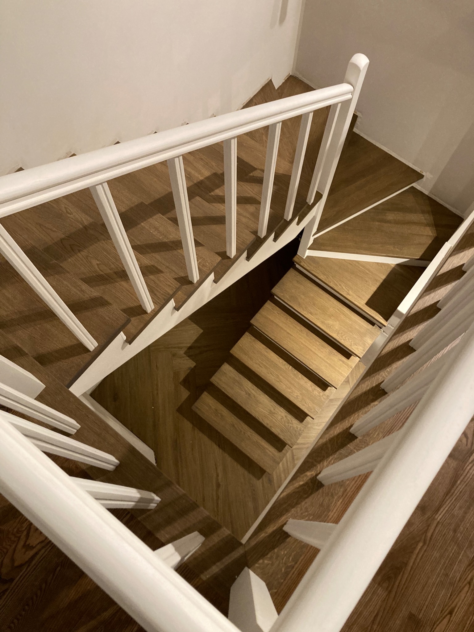 Widok z góry na drewniane schody z białymi balustradami, wykończone panelami imitującymi drewno w jodełkę.