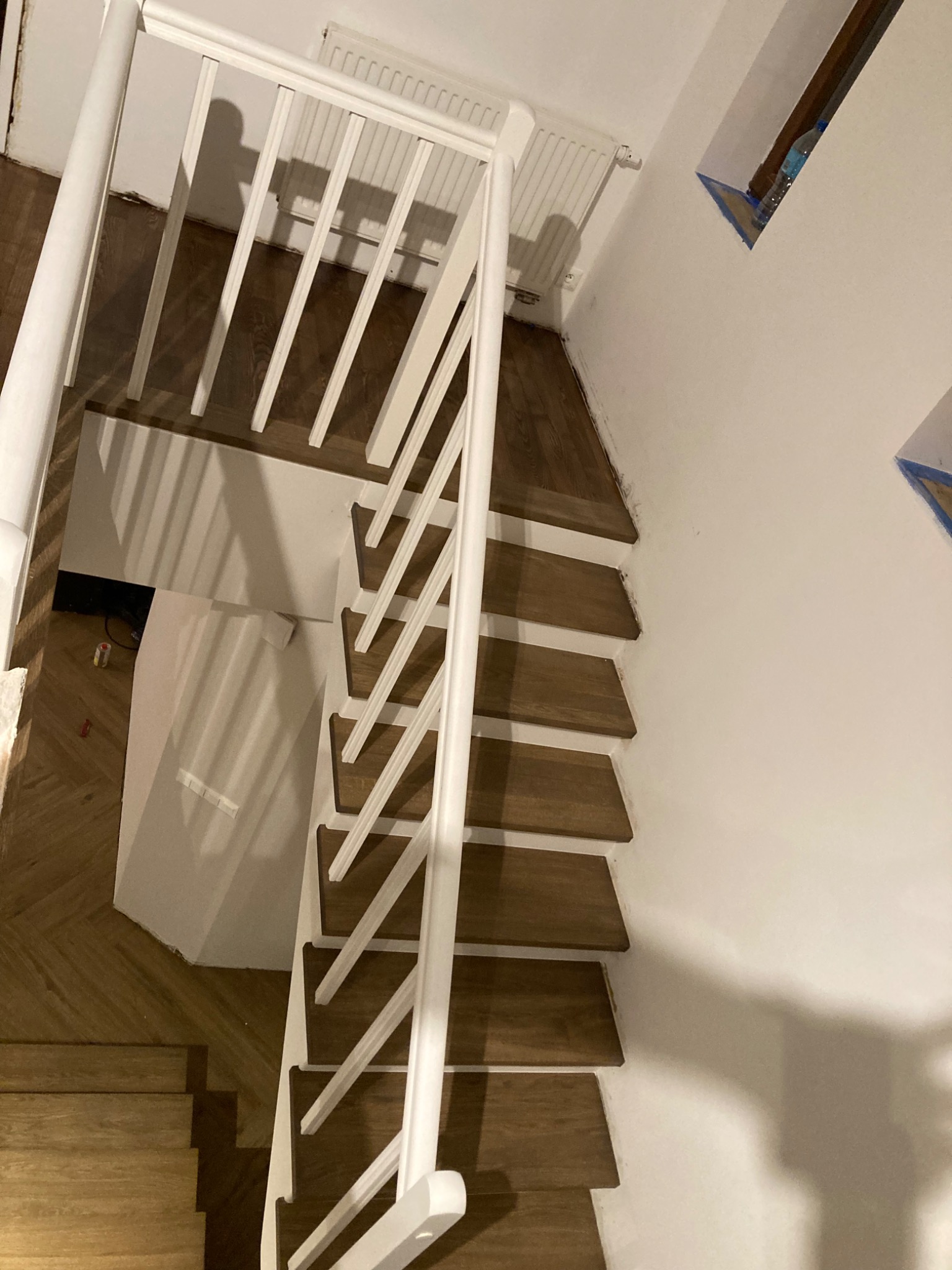 Widok z góry na drewniane schody z białymi barierkami, widoczne ślady po malowaniu na ścianie i podłodze, schody prowadzą w dół.