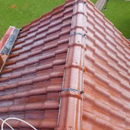 Czerwona dachówka ceramiczna pokryta kroplami wody po czyszczeniu, widok z góry na tle zielonego trawnika i ścieżki.