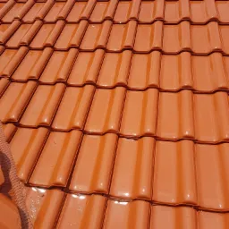 Błyszczące, pomarańczowe dachówki ceramiczne na dachu z widocznym oknem dachowym i elementami wentylacji kalenicy.