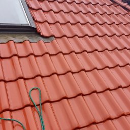 DGS - Czerwona dachówka ceramiczna z oknem dachowym i zieloną liną zabezpieczającą, widok z góry.