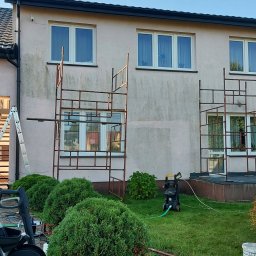 DGS - Dwukondygnacyjny budynek z jasną elewacją, częściowo umytą, z widocznymi rusztowaniami i myjką ciśnieniową na trawniku.