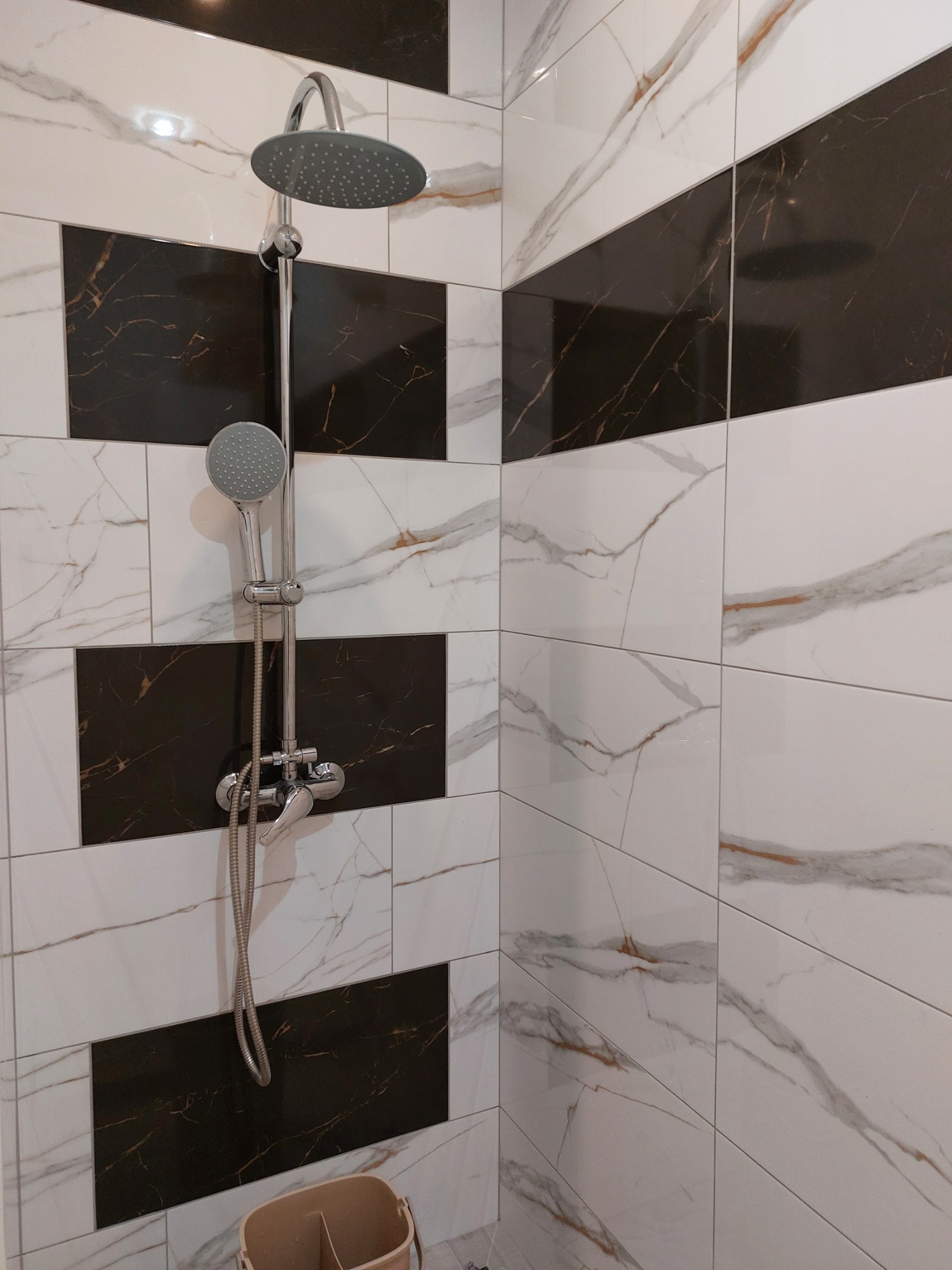 Nowoczesna kabina prysznicowa z dwoma rodzajami natrysku i dekoracyjnymi płytkami w kolorze białym z marmurkowym wzorem i czarnymi pasami.