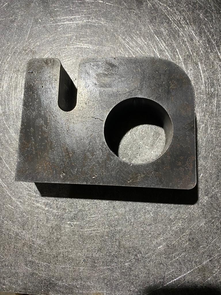 Szorstki element ze stali z wyciętym otworem i wcięciem, leżący na metalowej powierzchni z widocznymi śladami obróbki.