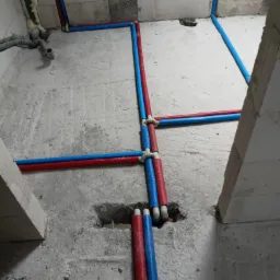 Rozprowadzenie instalacji wodnej i grzewczej w surowym stanie, rury w izolacji koloru czerwonego i niebieskiego, widoczne łączenia i fragmenty ścian z betonu komórkowego.