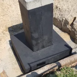 Betonowy fundament z hydroizolacją w wykopie, z wystającymi prętami i zabezpieczonymi kołkami, otoczony piaskiem i trawą.