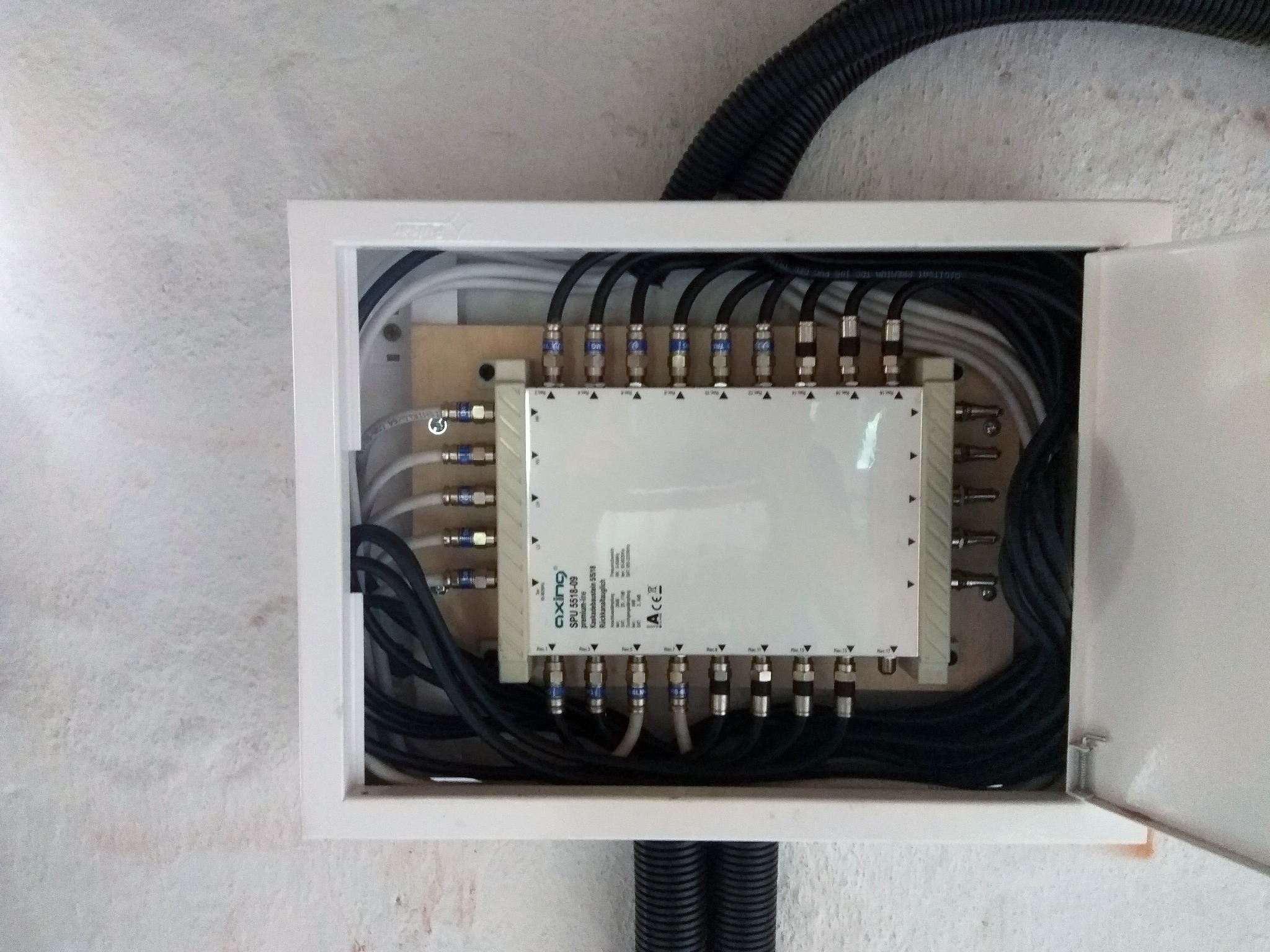 Rozdzielacz sygnału antenowego Axing SPI 5518-09 w białej skrzynce, z podłączonymi kablami koncentrycznymi, widoczne oznaczenia Rec 1-16, instalacja wewnątrz budynku.