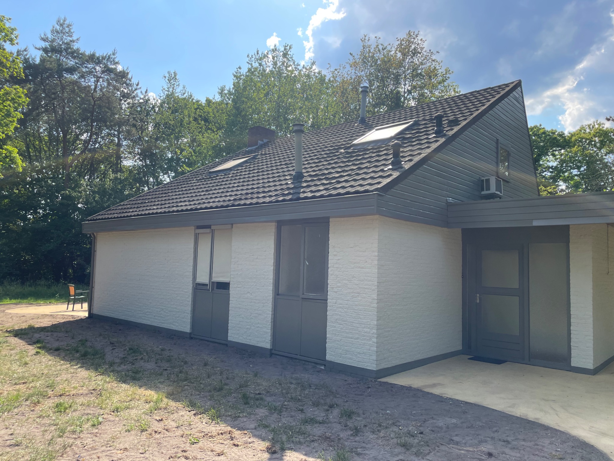 Odnowiony dom jednorodzinny z białą elewacją z cegły, szarą stolarką i ciemnoszarą dachówką, otoczony zielenią.