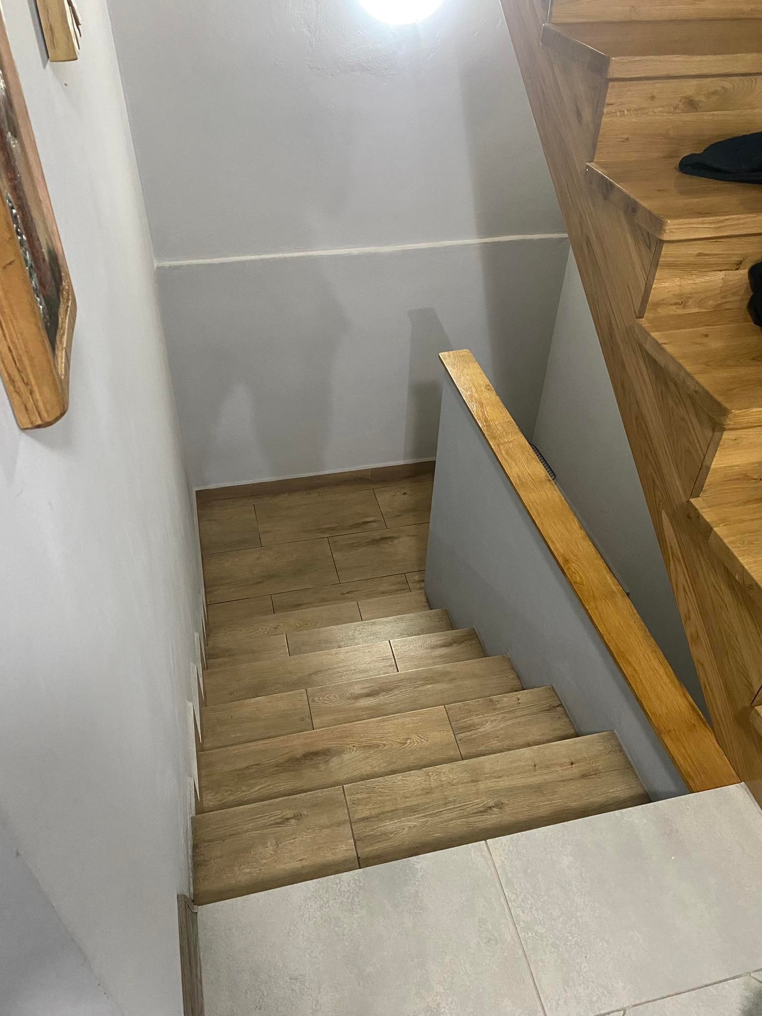 Wnętrze klatki schodowej z drewnianymi schodami wyłożonymi płytkami imitującymi drewno, szara ściana z drewnianą poręczą, widok z góry.