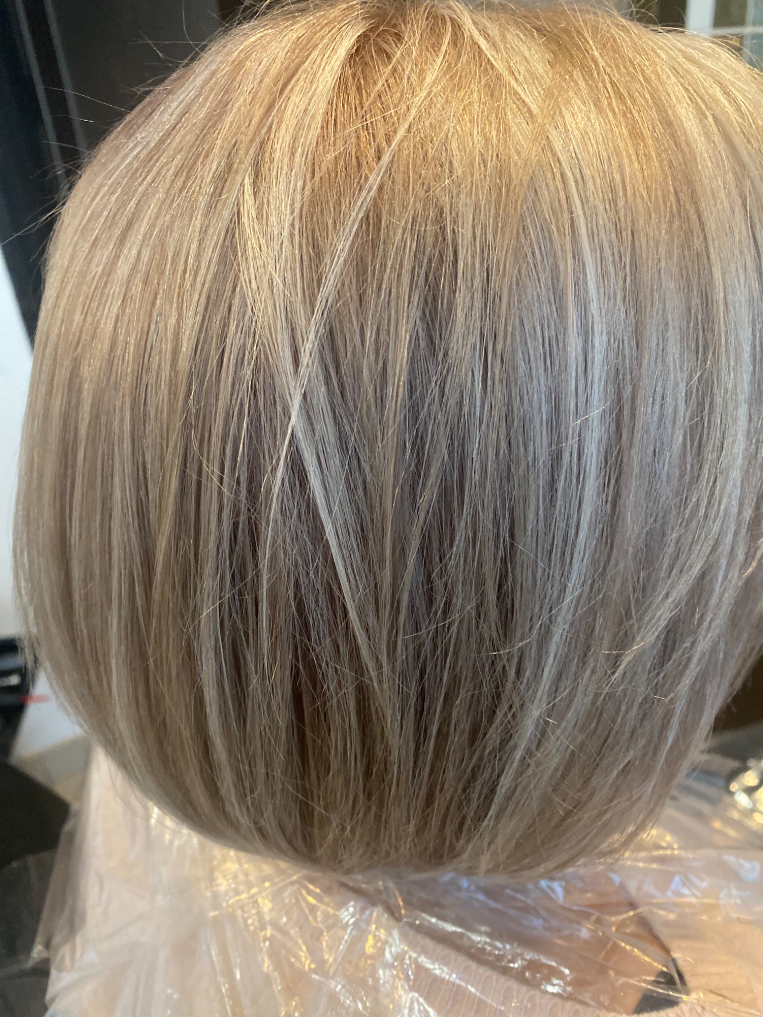 Krótkie, proste włosy w odcieniach blondu i szarości, widoczne po zabiegu koloryzacji, z plastikowym zabezpieczeniem na ramionach.