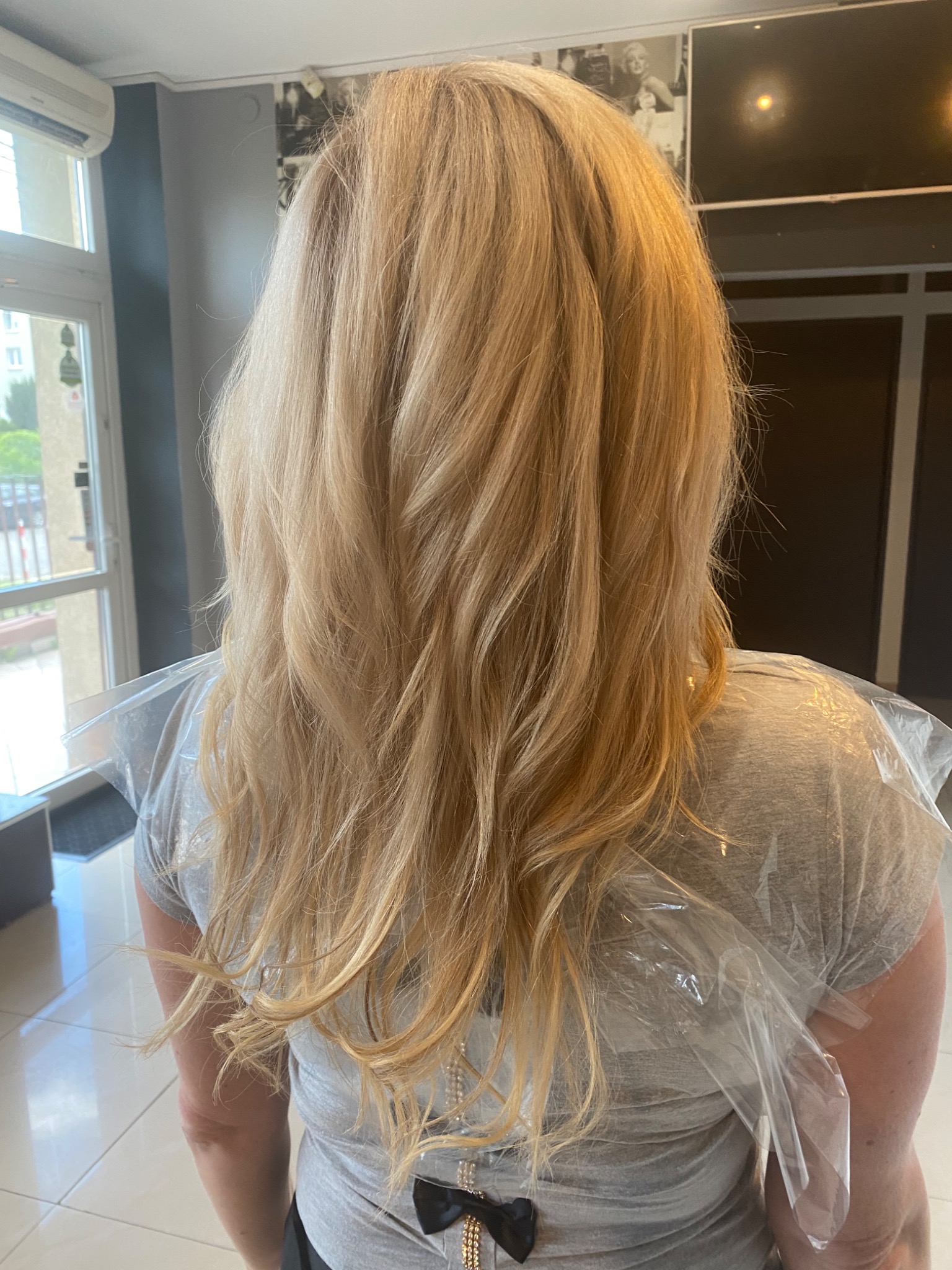 Widok z tyłu na blond włosy po koloryzacji, zabezpieczone peleryną ochronną w salonie.