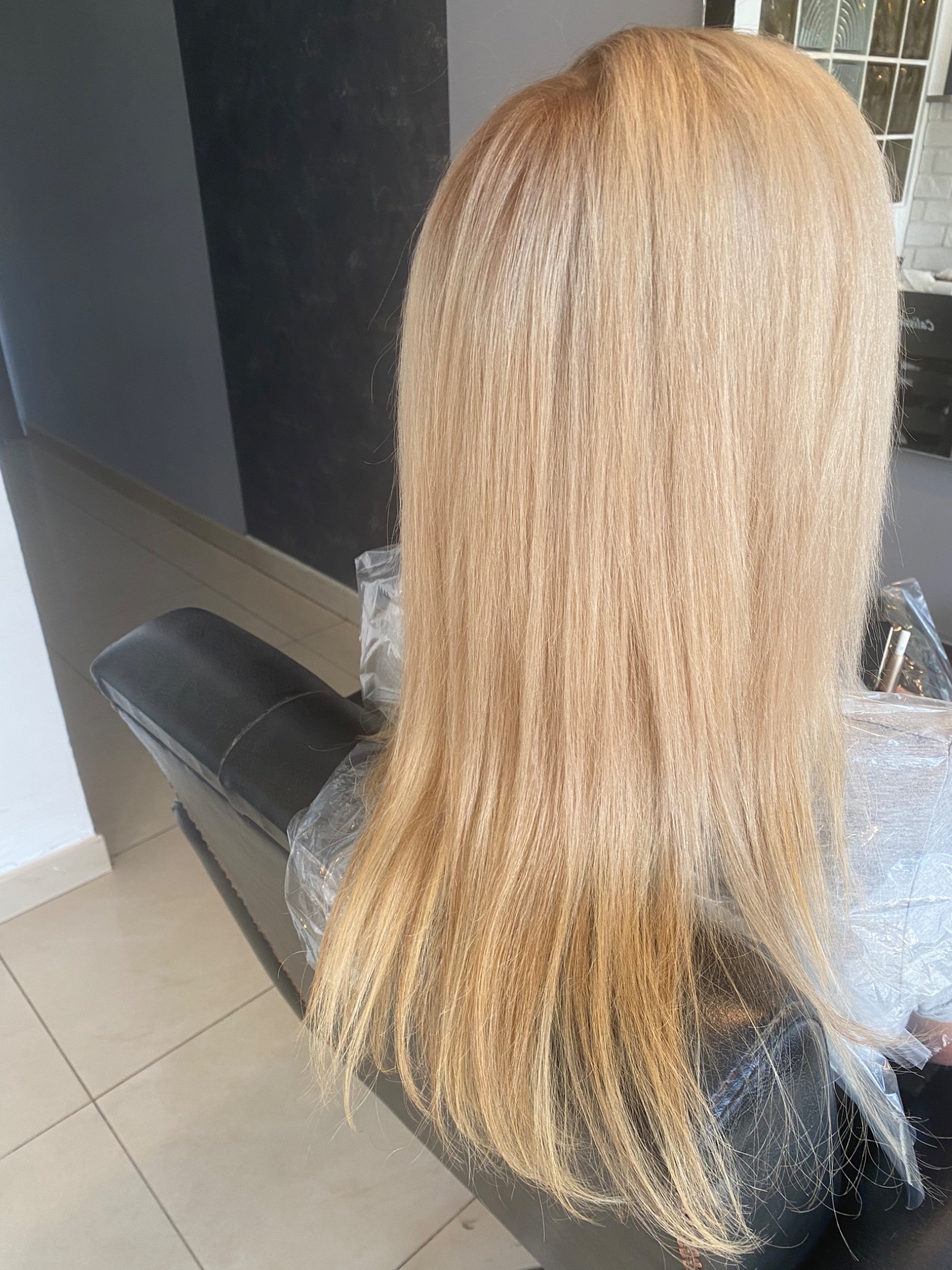 Świeżo farbowane, proste włosy blond, widoczne z tyłu, spoczywają na fotelu fryzjerskim zabezpieczonym folią.