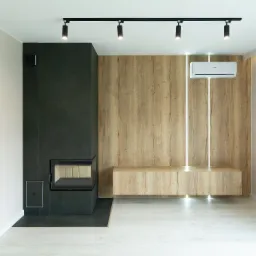 Nowoczesny salon z czarnym kominkiem, drewnianą ścianą z podświetleniem LED i klimatyzatorem, oświetlenie punktowe na suficie, jasna podłoga.