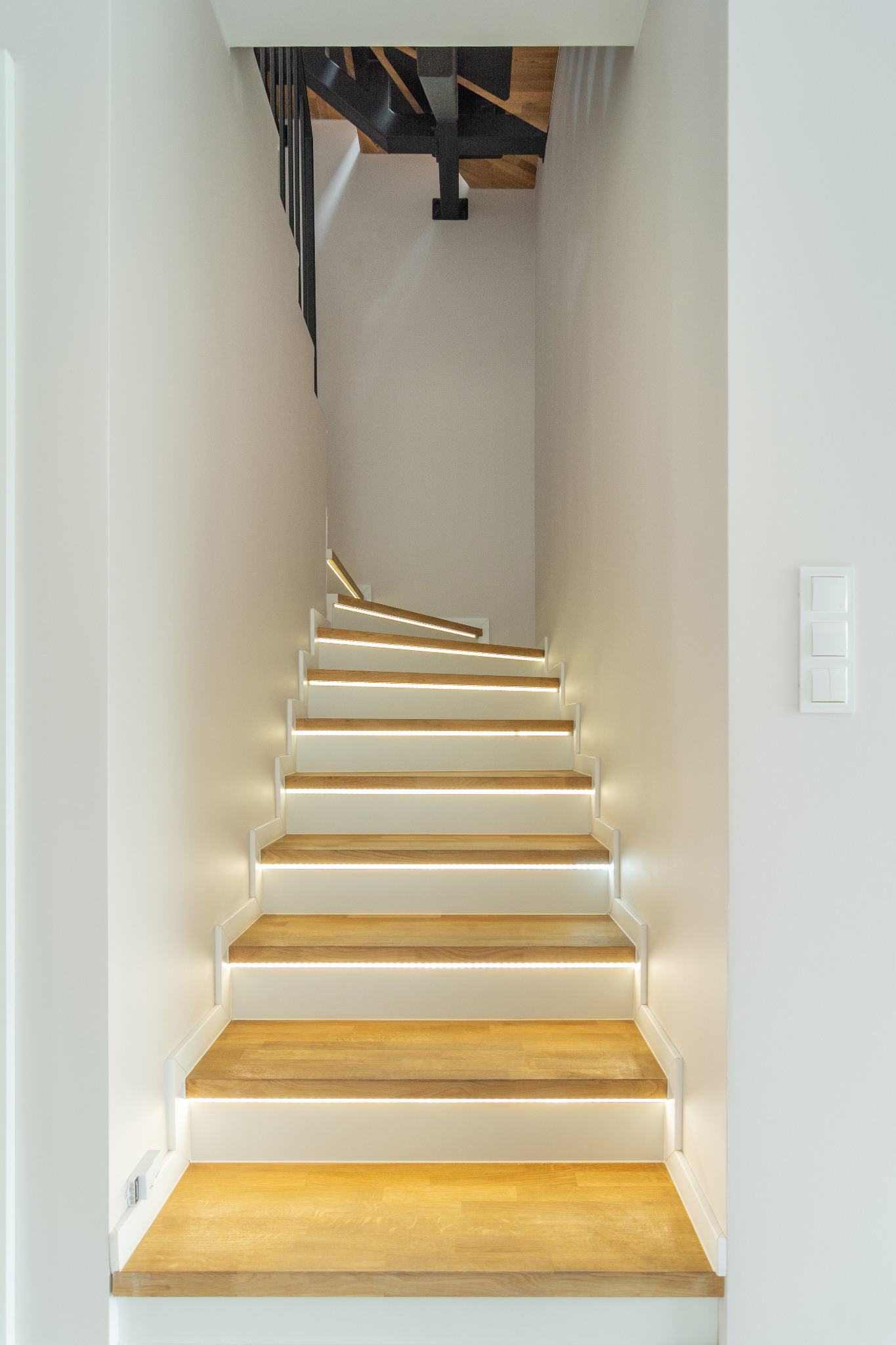 Nowoczesne schody drewniane z podświetleniem LED, białe ściany, minimalistyczny design, widok z dołu.