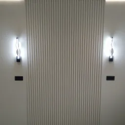 Ściana wykończona panelami pionowymi w kolorze beżowym, oświetlona od góry listwą LED i z dwoma nowoczesnymi kinkietami po bokach, z widocznymi gniazdkami elektrycznymi.